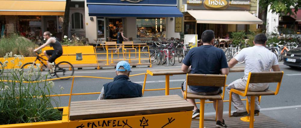 Passanten sitzen in einem Parklet an der Bergmannstraße in Kreuzberg.