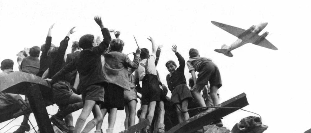 West-Berliner Jungen, die auf einem Trümmerberg stehen, winken einem US-Transportflugzeug zu (Aufnahme von 1948). 