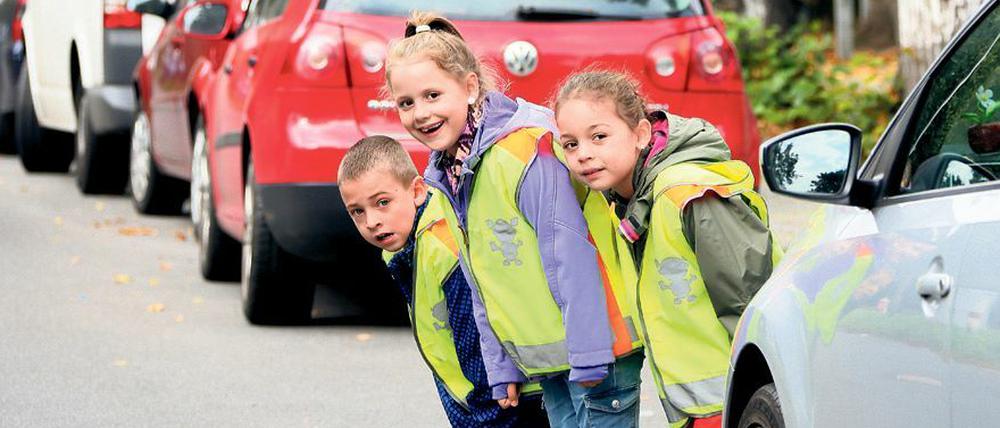 Kinder schauen auf dem Weg zur Schule hinter geparkten Autos hervor.