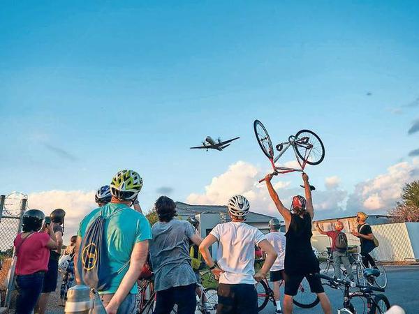 Grüne Zukunft. Die Fahrradfahrer des wöchentlichen „Night Ride“ grüßen ein landendes Flugzeug in der Küstenstadt.