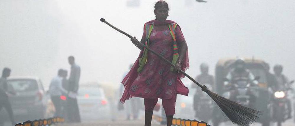 Eine Straßenkehrerin arbeitet im Smog von Delhi.