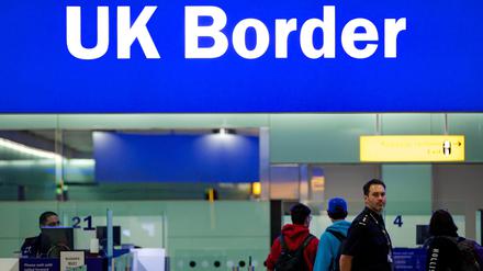 Grenzbeamte stehen am Flughafen London-Heathrow unter einem Schild mit der Aufschrift „UK Border“ (Grenze des Vereinigten Königreiches).