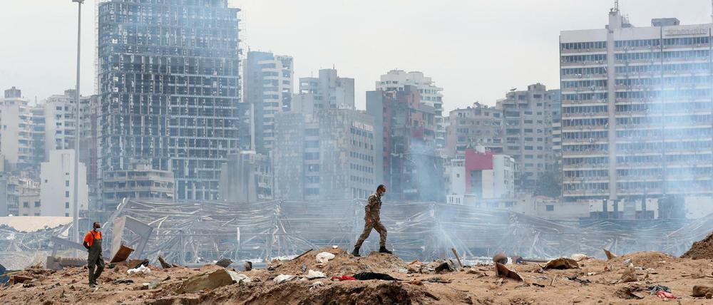 Ein Soldat geht über den Ort einer Explosion im Hafen, während im Hintergrund schwer beschädigte Gebäude zu sehen sind.