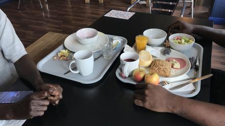 Ein geflüchteter Nigerianer und ein Tourist aus Budapest frühstücken in einem Hostel im Prenzlauer Berg. Sie haben sich an der Essensausgabe kennengelernt.