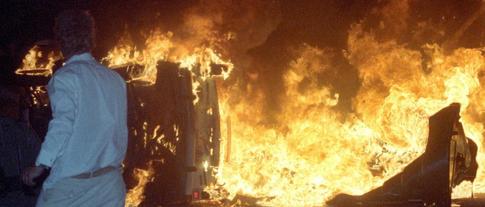  Ein Mann steht 27.08.1992 vor einem brennenden Pkw auf einer Straße am zentralen Asylbewerberheim von Mecklenburg-Vorpommern in Rostock-Lichtenhagen. 