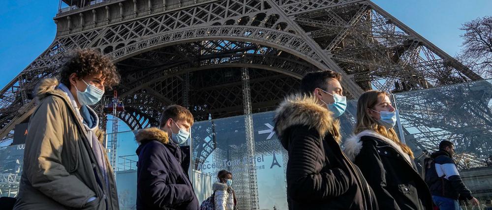 Menschen tragen Schutzmasken und gehen am Eiffelturm vorbei. 