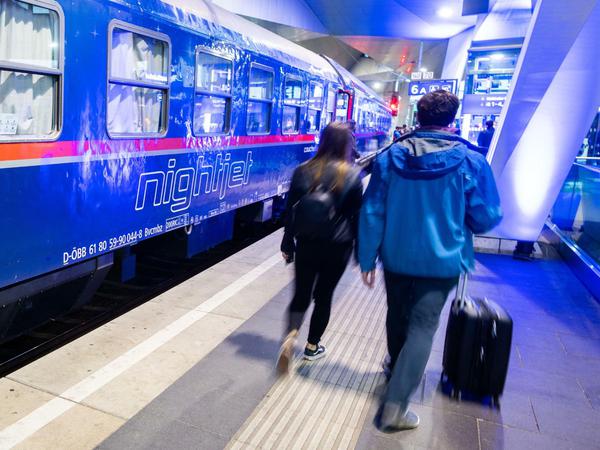 Passagiere gehen neben einem Nightjet Zug der ÖBB auf einem Gleis im Wiener Hauptbahnhof. 