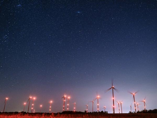 Sterne leuchten am Nachthimmel eines hell beleuchteten Windenergieparks im brandenburgischen Petersdorf.