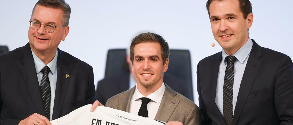 DFB-Präsident Reinhard Grindel (l) und Generalsekretär Friedrich Curtius (r) überreichen dem neuen DFB-Ehrenspielführer Philipp Lahm ein Trikot.