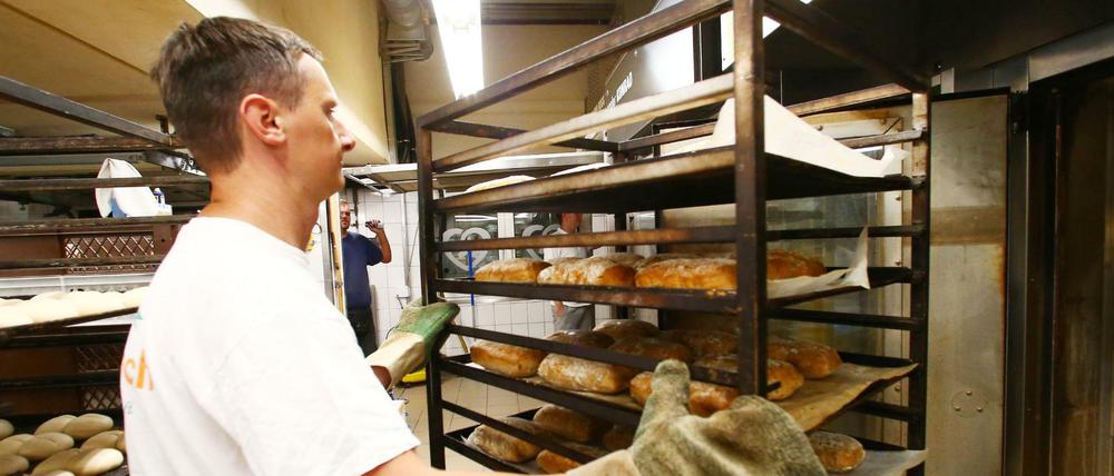 Ein Bäcker holt frisch gebackene Brote aus einem Backofen in einer Bäckerei. 