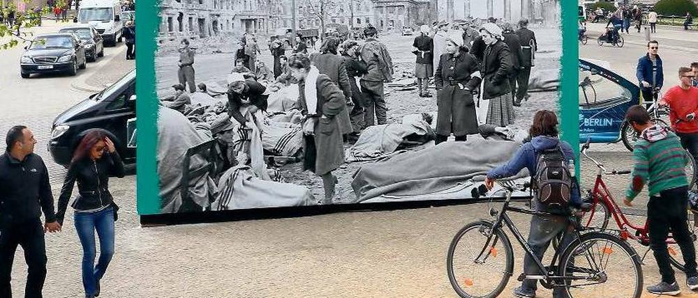 Auf dem Pariser Platz vor dem Brandenburger Tor betrachten Menschen ein Plakat, dass den Platz im Frühjahr 1945 zeigt.