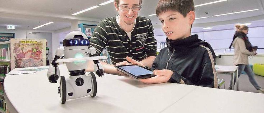 Ein Bibliotheksmitarbeiter erklärt einem Jungen Besucher die Fernsteuerung eines Miniroboters mittels Tablet.