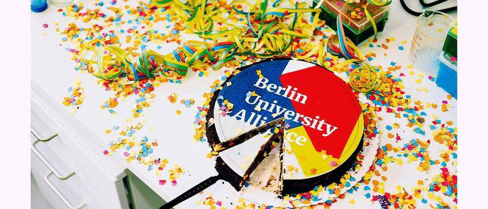 Eine Torte mit der Aufschrift Berlin University Alliance steht auf einem Schreibtisch, der mit Luftschlangen und Konfetti bedeckt ist.