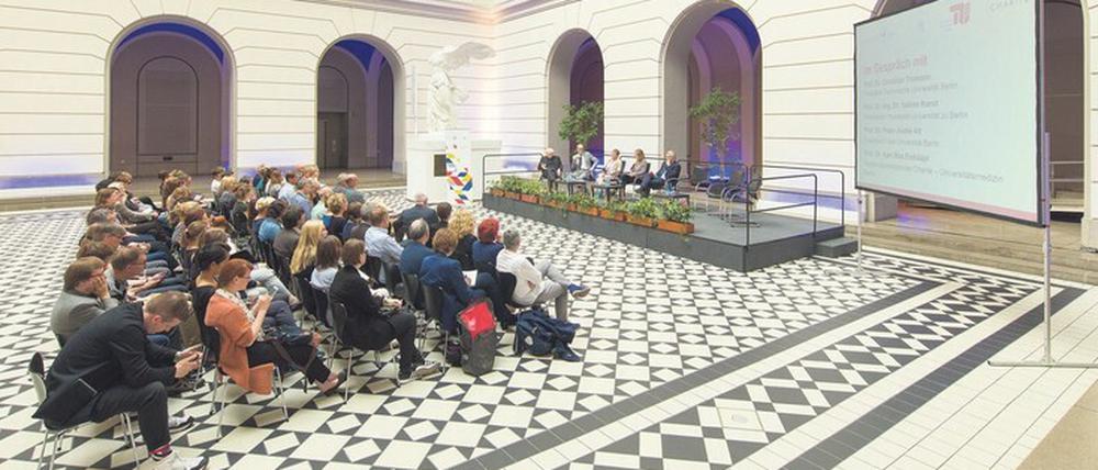 Im Lichthof der TU Berlin nehmen Wissenschaftler:innen an einer Podiumsdiskussion vor Publikum teil.