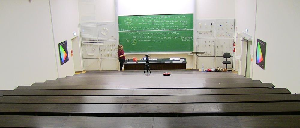 In einem Hörsaal steht eine Dozentin erklärend vor einer Tafel mit Formel, dabei wird sie gefilmt.